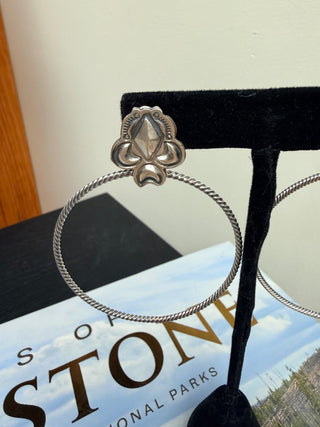 Handmade sterling silver hoop earring with decorative concho top on black display stand