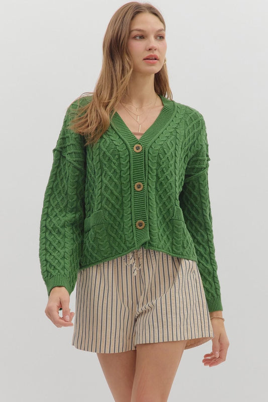Woman wearing a green knitted cardigan over a striped skirt on a plain background