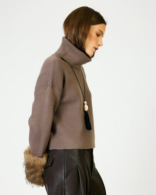 Mocha turtleneck sweater with fur cuffs and tassel necklace, paired with dark leather pants.