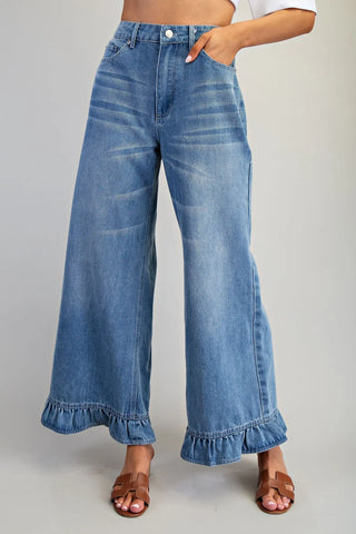 Blue jeans with ruffled cuffs worn by a person on a plain background