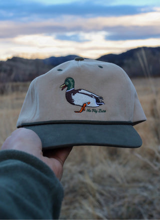 Beige cap with duck design held in front of a scenic landscape