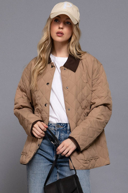 Woman wearing a beige quilted jacket, white shirt, blue jeans, and beige cap on a gray background
