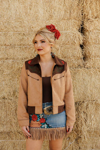 Woman wearing a tan jacket with floral accents in front of hay bales