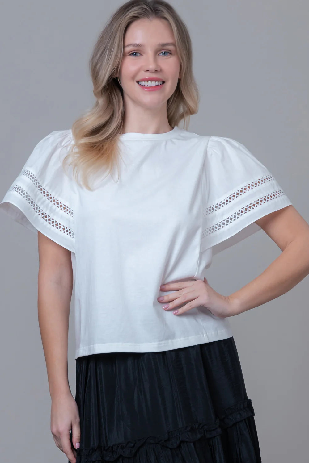 Woman wearing a white blouse with lace sleeves against a gray background