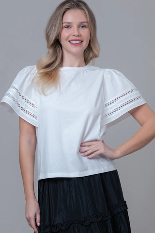 Woman wearing a white blouse with lace sleeves against a gray background