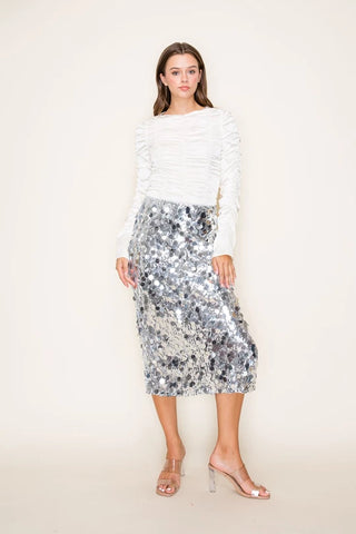 Woman wearing a white lace top and sequin skirt on a plain background