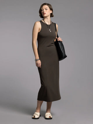 Woman wearing a brown sleeveless dress holding a black handbag against a gray background