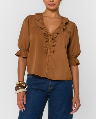 Woman wearing a brown blouse with ruffled details and blue jeans on a white background
