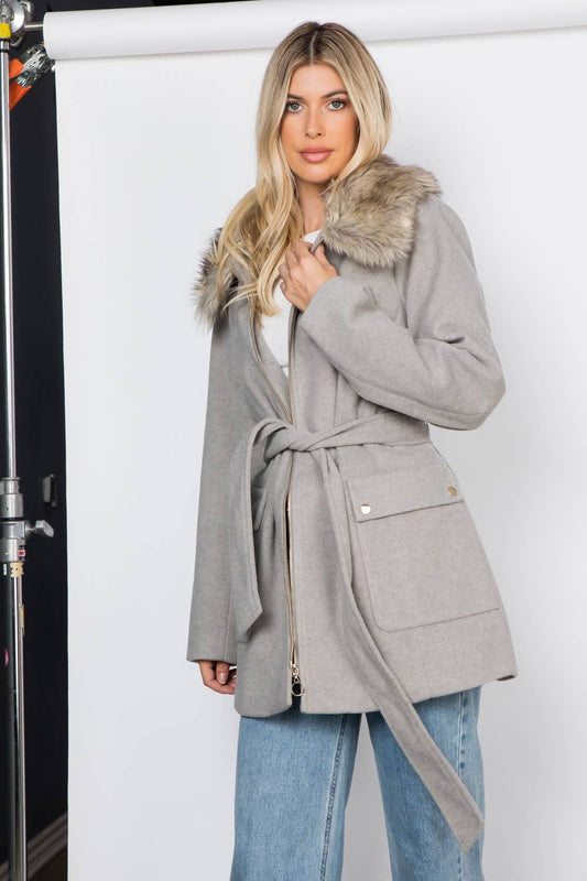 Woman wearing a gray coat with fur collar against a white background
