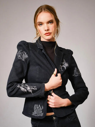 Woman wearing a black jacket with white embroidery on a gray background