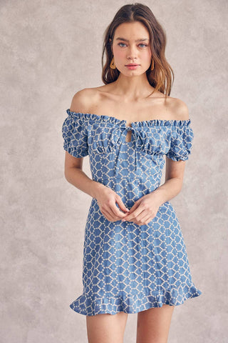 A woman wearing a blue denim mini dress with eyelet details, ruffles, and a drawstring.