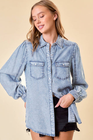 Woman wearing a light blue denim shirt with ruffled sleeves on a beige background