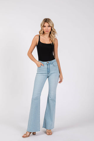 Woman wearing light blue flared jeans and a black top on a white background