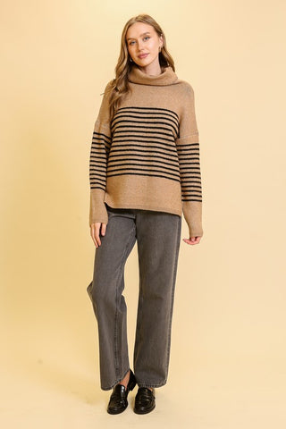 Woman wearing a beige sweater with black stripes and gray pants on a beige background