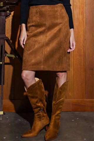 Person wearing a brown suede skirt and matching knee-high boots against a wooden background