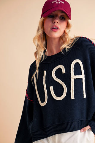 A woman wearing a navy blue sweater with the letters 'USA' in bold white letters on the front.