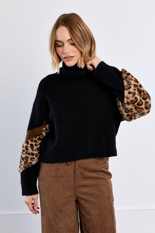 Model wearing black turtleneck knit sweater with leopard print faux fur sleeves and brown trousers