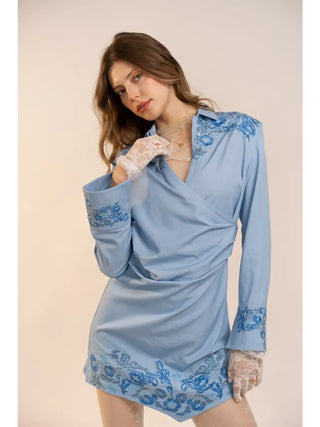 Woman wearing a light blue dress with floral embroidery on a beige background