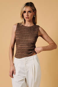 Woman wearing a brown textured top and white pants against a beige background