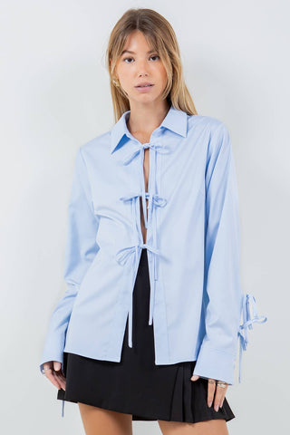 Woman wearing a light blue shirt with tie details on a white background