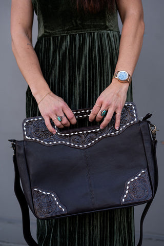 Person holding a brown handbag with decorative elements against a gray background