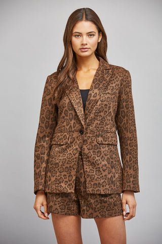 A woman modeling a brown and black leopard print blazer and matching shorts set against a solid gray studio background.