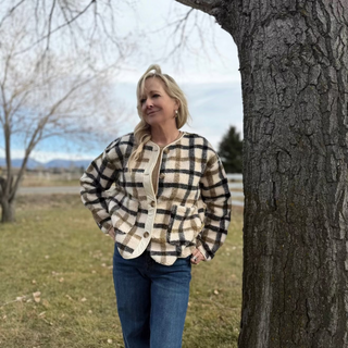 Woman wearing a plaid jacket and jeans standing next to a tree in an outdoor setting