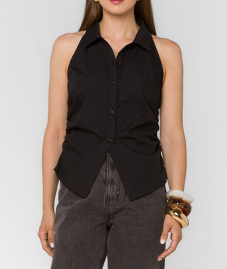 Woman wearing a black sleeveless button-up shirt with a plain background