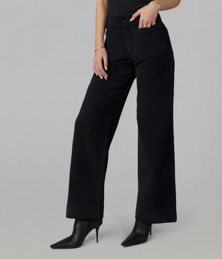 Model wearing high rise wide leg black corduroy pants with front patch pockets and black heeled boots