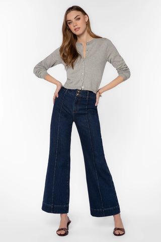 A woman modeling a light gray long-sleeve henley top and dark blue wide-leg denim jeans against a plain white studio background.