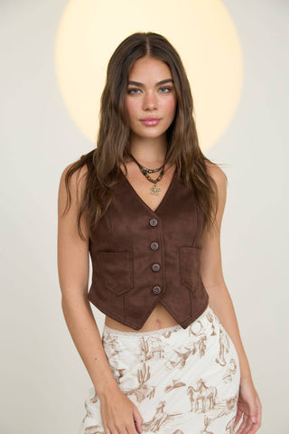 Woman wearing a brown vest over a patterned skirt with a neutral background