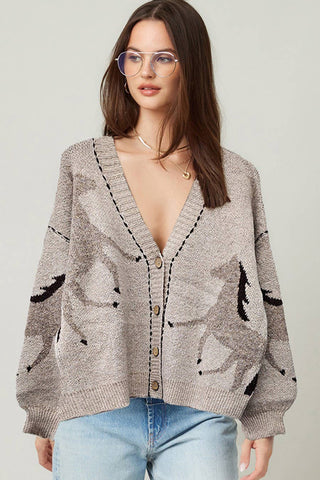 Woman wearing a patterned cardigan over a sheer top with a plain background