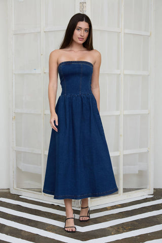 Woman wearing a blue strapless dress standing against a white wall.