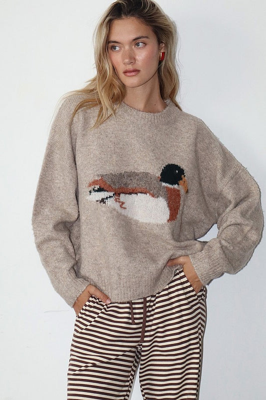 Woman wearing a beige sweater with a bird design on a plain background