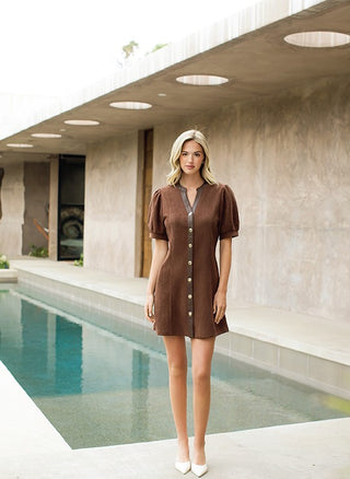 Woman in a brown dress standing by a pool with a modern building in the background