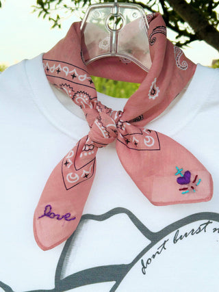 Pink bandana with black patterns and purple text on a white shirt with black text.