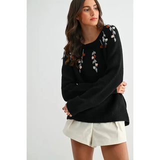 Woman wearing a black sweater with floral embroidery on a white background