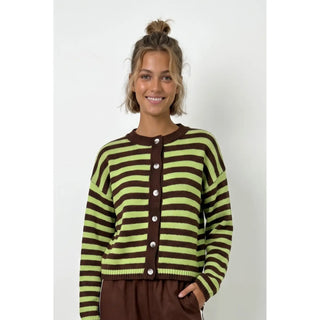 A woman wearing a brown and lime green striped knit cardigan with a button-up front, paired with brown bottoms, standing against a light gray studio background.