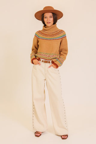 Woman wearing a patterned sweater and wide-leg jeans on a beige background