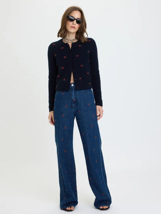 A model wearing a dark navy cropped cardigan with small red embroidered motifs, paired with high-waisted blue wide-leg jeans featuring a similar red embroidered pattern, set against a plain white studio background.