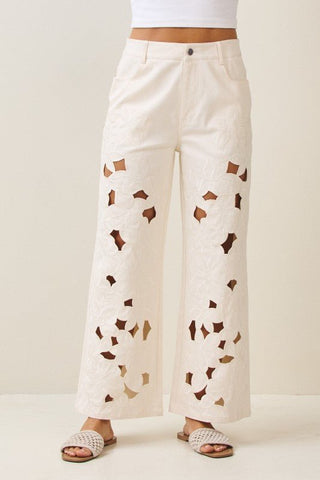 White pants with brown geometric patterns worn by a person on a white background