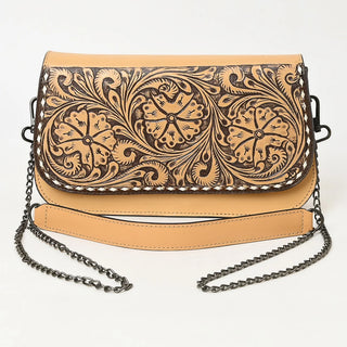 A tan leather shoulder bag with dark brown tooled floral and scroll patterns on the front flap, featuring a matching tan leather strap and a dark metal chain strap, shown against a plain white background.