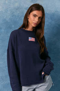 Woman wearing a navy blue sweatshirt with a small flag patch on a blue textured background