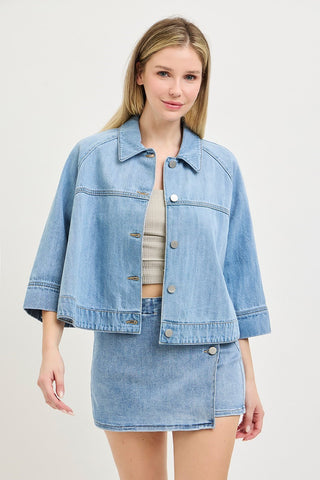 Woman wearing a light blue denim jacket and skirt on a plain background