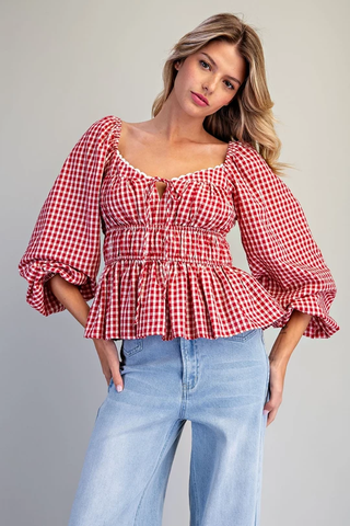 Woman wearing a red and white checkered blouse with blue jeans on a gray background