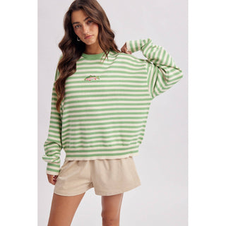 Woman wearing a green and white striped sweater with beige shorts on a light gray background