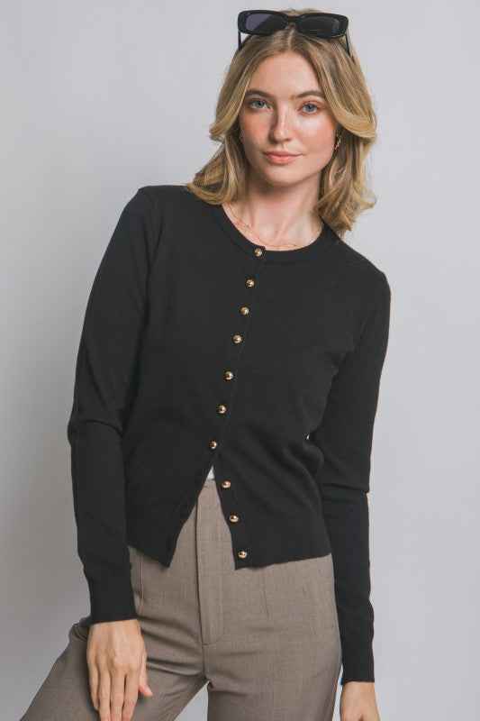 Woman wearing a black cardigan with gold buttons on a plain background