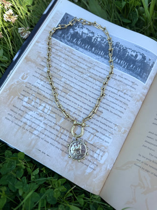 Gold necklace with a pendant on an open book in a grassy setting