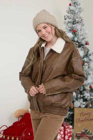Woman wearing a brown leather jacket with a Christmas tree and presents in the background