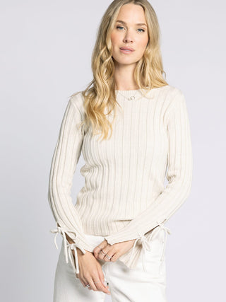 Woman wearing a white ribbed sweater with long sleeves against a light gray background